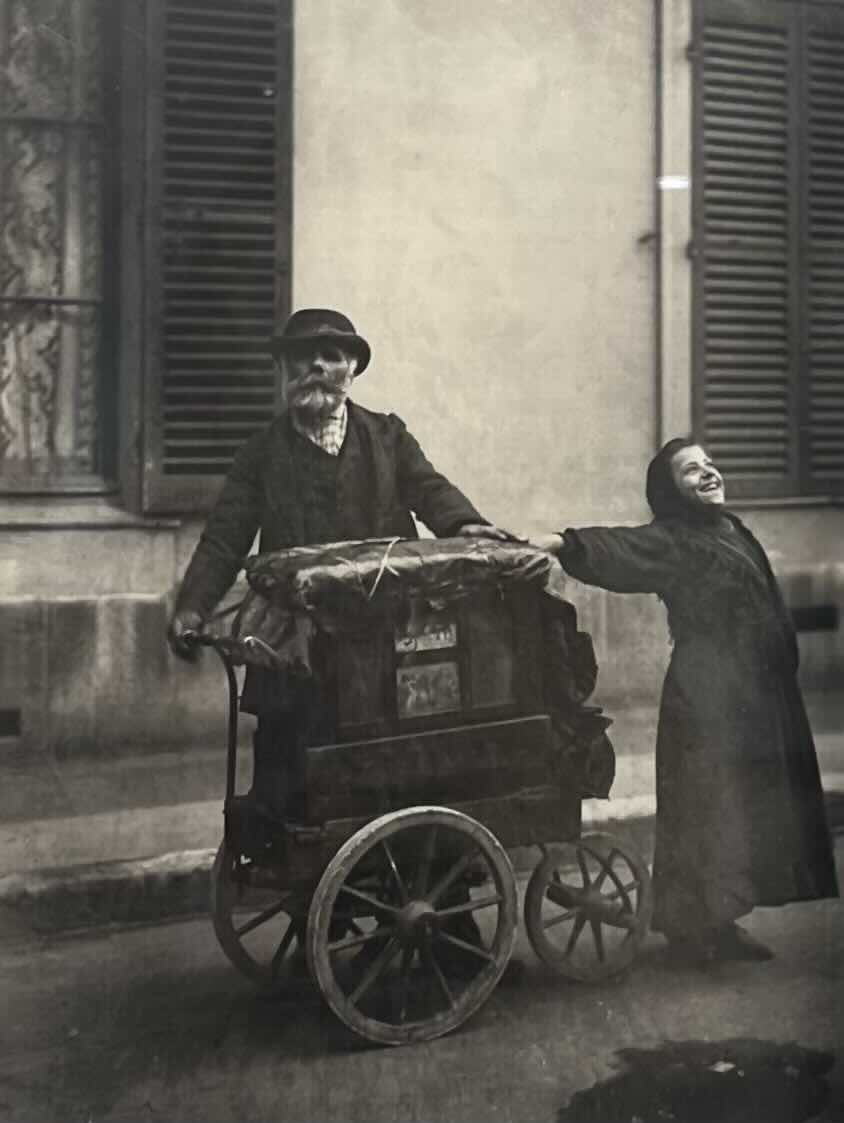 This gelatin silver print brings together the legacies of two pioneering photographers. Atget devoted his career to documenting “Old Paris,” creating an extraordinary photographic record of its streets, architecture, interiors, and vanishing trades. This work belongs to his series of petits métiers—images of Parisian street workers posed with the tools and attributes of their trades. In this image, the organ-grinder’s solemn gaze contrasts with the exuberant energy of the child beside him, capturing a fleeting, wonderfully human moment of street life in turn-of-the-century Paris.