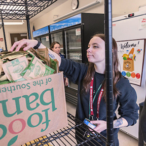 A young woman packs a food bank box.