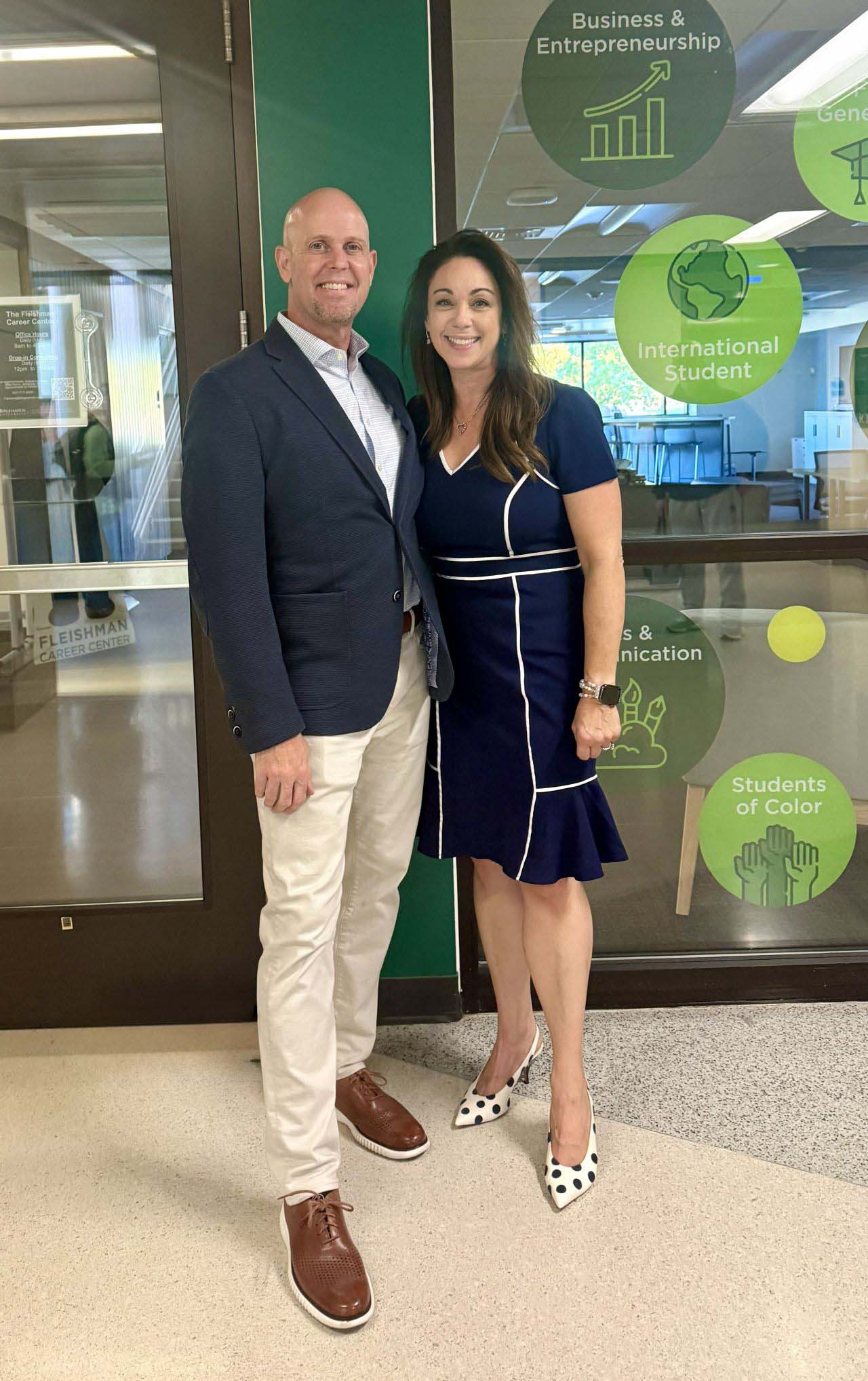 Dan Black and Lisa Black stand together smiling inside the Fleishman Center for Career and Professional Development, with green graphics on the glass walls behind them.