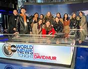 Students at a NYC CONNECT Employer Trek at ABC News. They are standing behind the news anchor desk and smiling.
