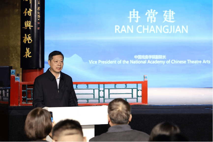 中国戏曲学院副院长冉常建在讲台上致闭幕辞。他身后的蓝色大屏幕上用中英文显示着他的姓名和职称。
