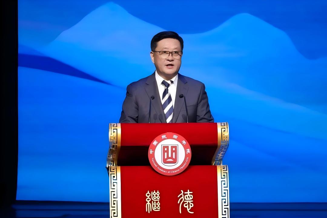 院长尹晓东身着西装、佩戴条纹领带子站在舞台中央,在印有“中国戏曲学院”校徽的红色讲台后发表讲话。