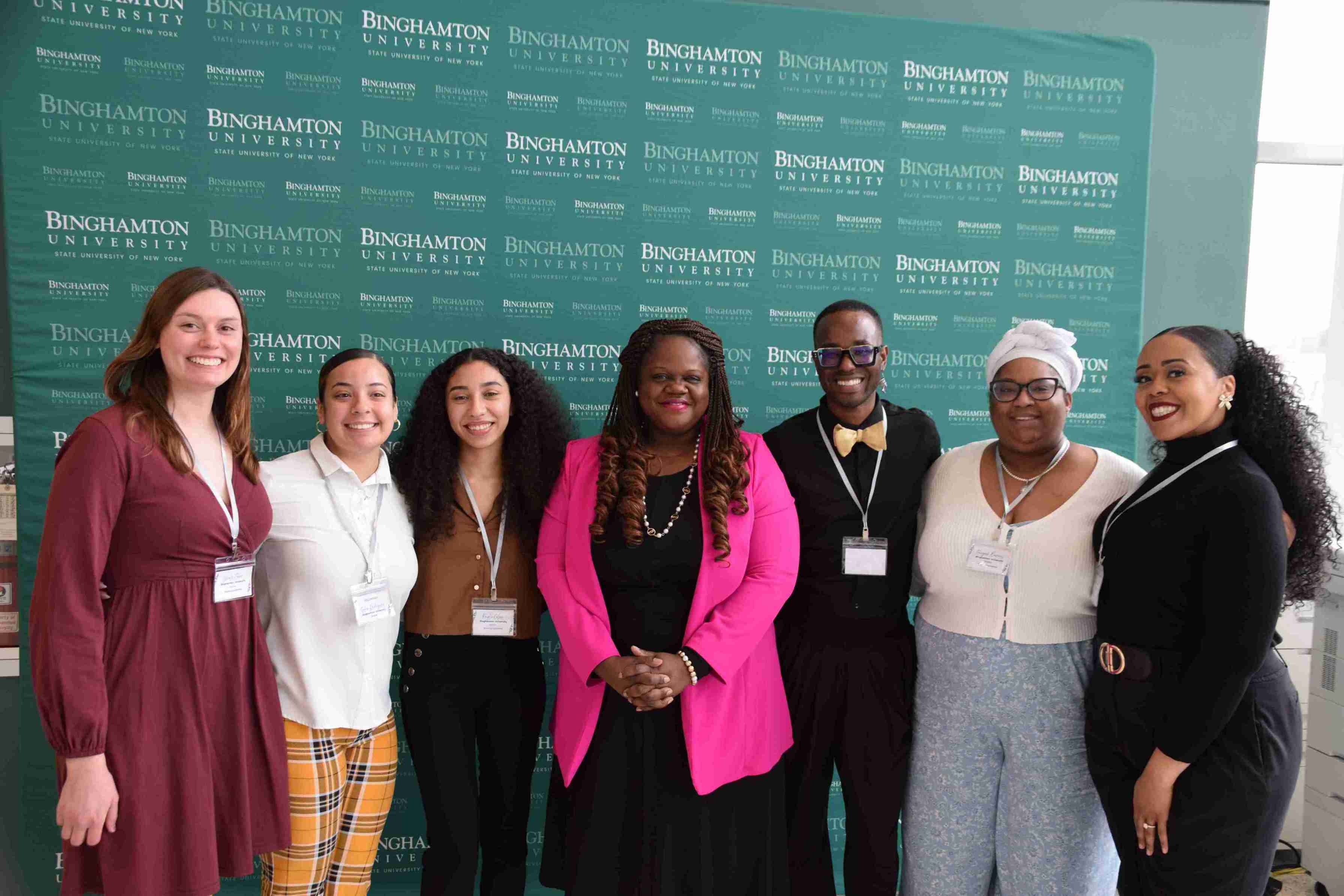 Six people, with Senator Lea Webb in the middle, gathered in front of a Binghamton University backdrop.