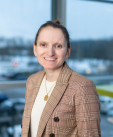 Image of a women smiling for a picture with a plaid business jacket white shirt and round necklace