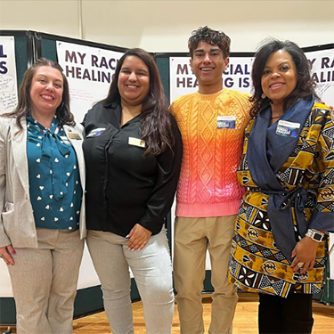 A diverse group of employees stand with arms around one another.