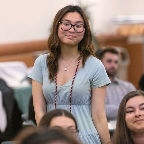 a young Asina woman in a blue dress stands during an assembly