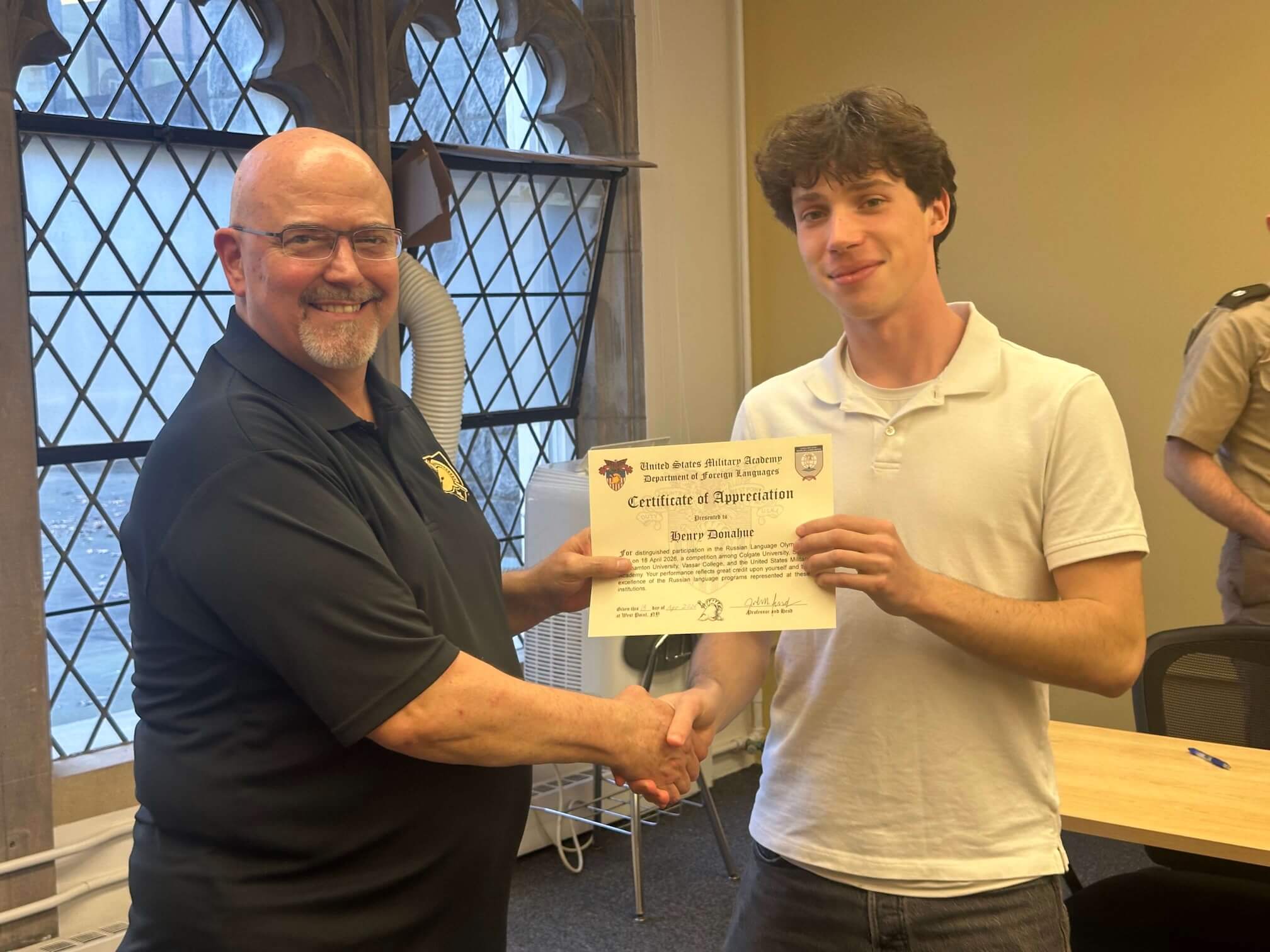 A student and a professor shaking hands and exchanging an award certificate