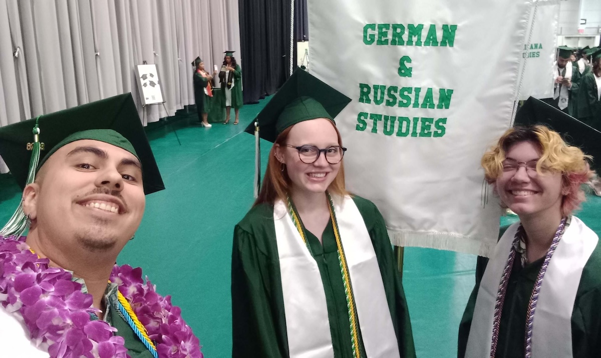 Three college graduates posing in front of a sign that says "German & Russian Studies"