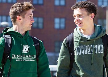 Two Binghamton University students walking across campus and talking between classes.