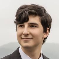 Shoulders-up headshot of a young man with short brown hair wearing a suit