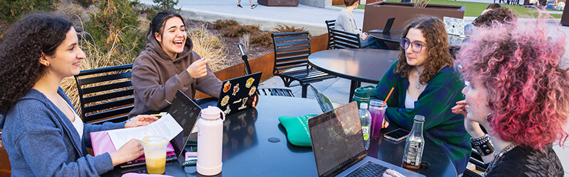 A group of students sit at a table outside Bartle Library, appearing to have a lively discussion
