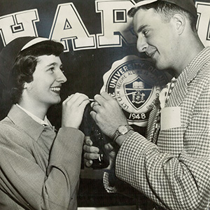 Two students share a soda in front of the Harpur logo