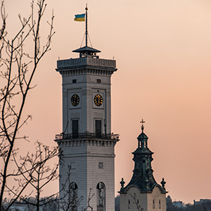 A white concrete clocktower topped with the Ukrainian flag