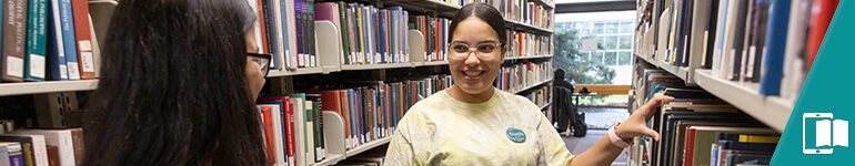 Two students talking and smiling as they look through the stacks in the Science Library