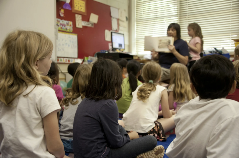 Photo of a teacher holding up a book in front of a classroom