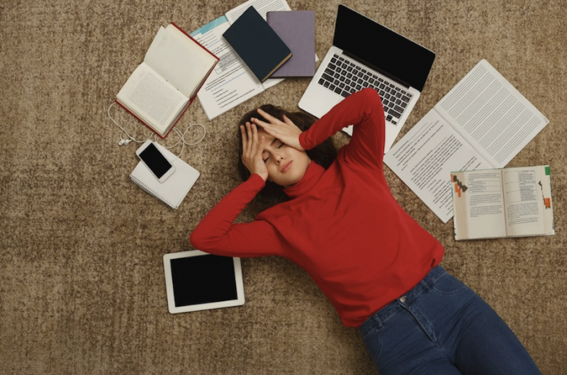 Photo of a teenager lying on the floor looking stressed next to a computer and books