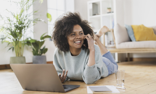 Photo of a woman lying on a floor talking on the phone in front of a laptop