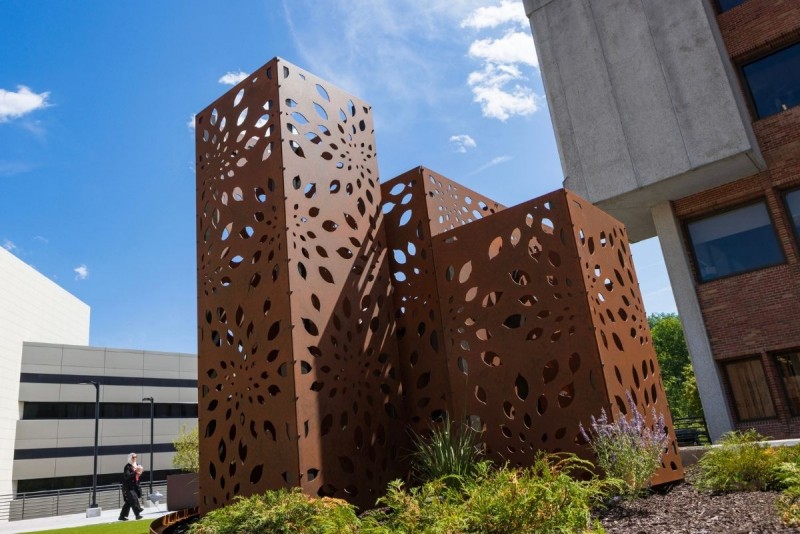 New floral-themed art panels are shown next to a building on campus on a sunny day.