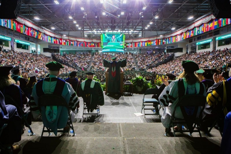 President Harvey Stenger is shown from behind on stage at Commencement with his arms raised in excitement.
