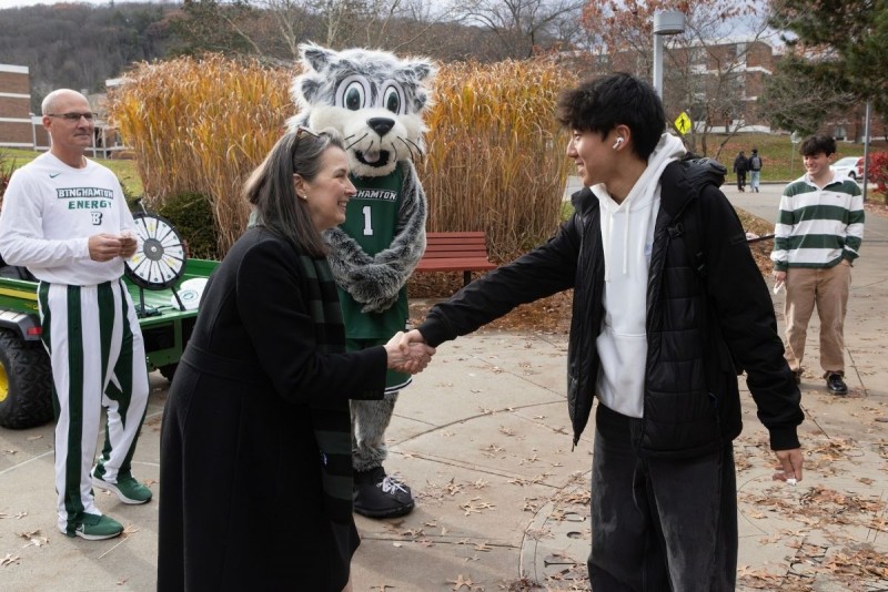 President Anne shakes the hand of a student outside on campus.