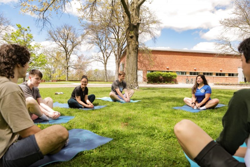 Students sit in a yoga pose outside in a circle