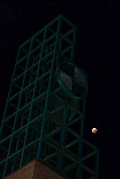 The moon appears red as it's seen in the night sky over the clock tower.