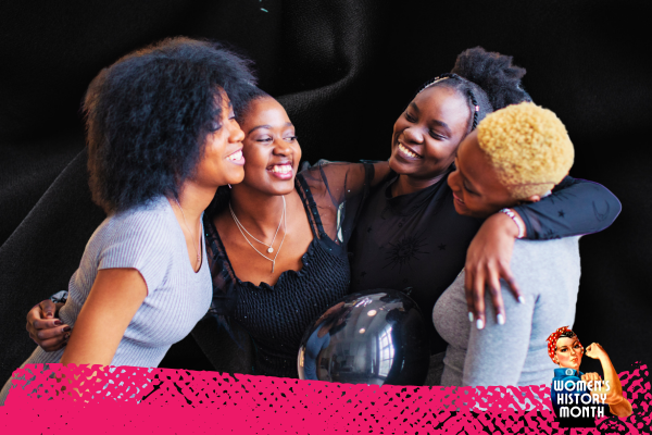 An image of a group of woman of color standing in a circle with their arms around one another.