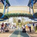 Individuals speak to a crowd at a children's playground during a ribbon-cutting ceremony.