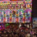 Crowd watches abstract 2D art projection on building.