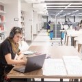 A student wearing headphones sits at a table in the library, studying.