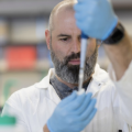 Photo of Matthew Emery wearing a lab coat and piping into a test tube