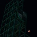 The moon appears red as it's seen in the night sky over the clock tower.
