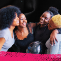 An image of a group of woman of color standing in a circle with their arms around one another.