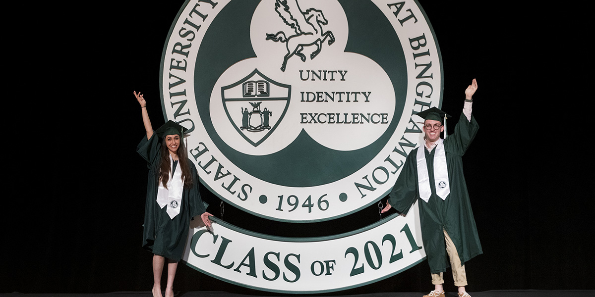 Maya Kallman ’21, intern in the Office of the President, who will receive double degrees in business administration and graphic design, and Zachary Herz ’21, student representative to the Binghamton University Council, who will receive a degree in psychology, pose with the large University seal following the taping of the 2021 Virtual Commencement Ceremony.