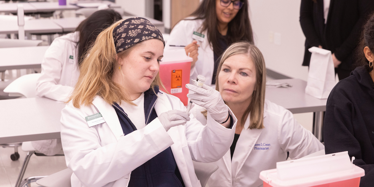 Karen Conn, manager of The Medicine Shoppe in Binghamton, instructs first-year student Christina Schnee on how to prepare a syringe for immunizing as part of the American Pharmacists Association (APhA) Immunization Delivery Certificate Program.