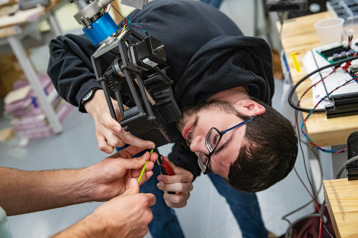 Binghamton University Rover Team member Noah Randman leans in to adjust the rover's gripper component in the Fabrication Lab at the Engineering Building this spring.