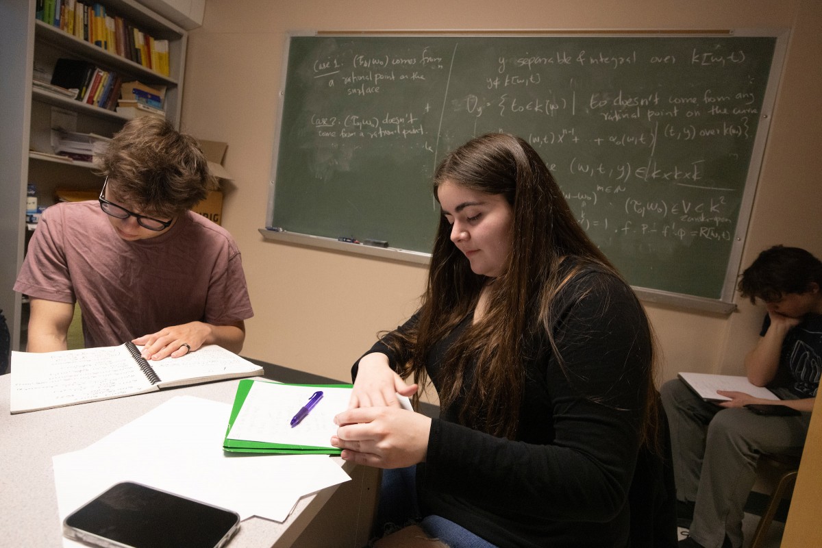 Associate Professor of Mathematics and Statistics Alexander Borisov hosts a problem-solving session on the evening of March 26, 2024, at his Whitney Hall office, where students participating in the William Lowell Putnam Mathematical Competition practice their skills. Pictured here, students Nikita Safronov, Blanca Parker and Josiah Moltz solve a problem.