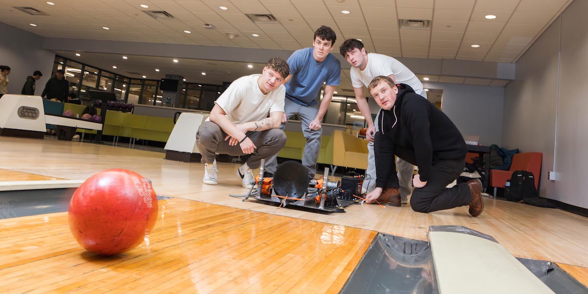 Mechanical engineering seniors, from left, Kyle Blair, Matthew Kershaw, Liam Heanue and Dan Ahern test their senior project — a bowling robot — at the bowling alley in the Union Undergrounds. Six robots competed at the end of the semester as part of the Mechanical Engineering Senior Capstone Expo, and this team came in first place with a score of 135.