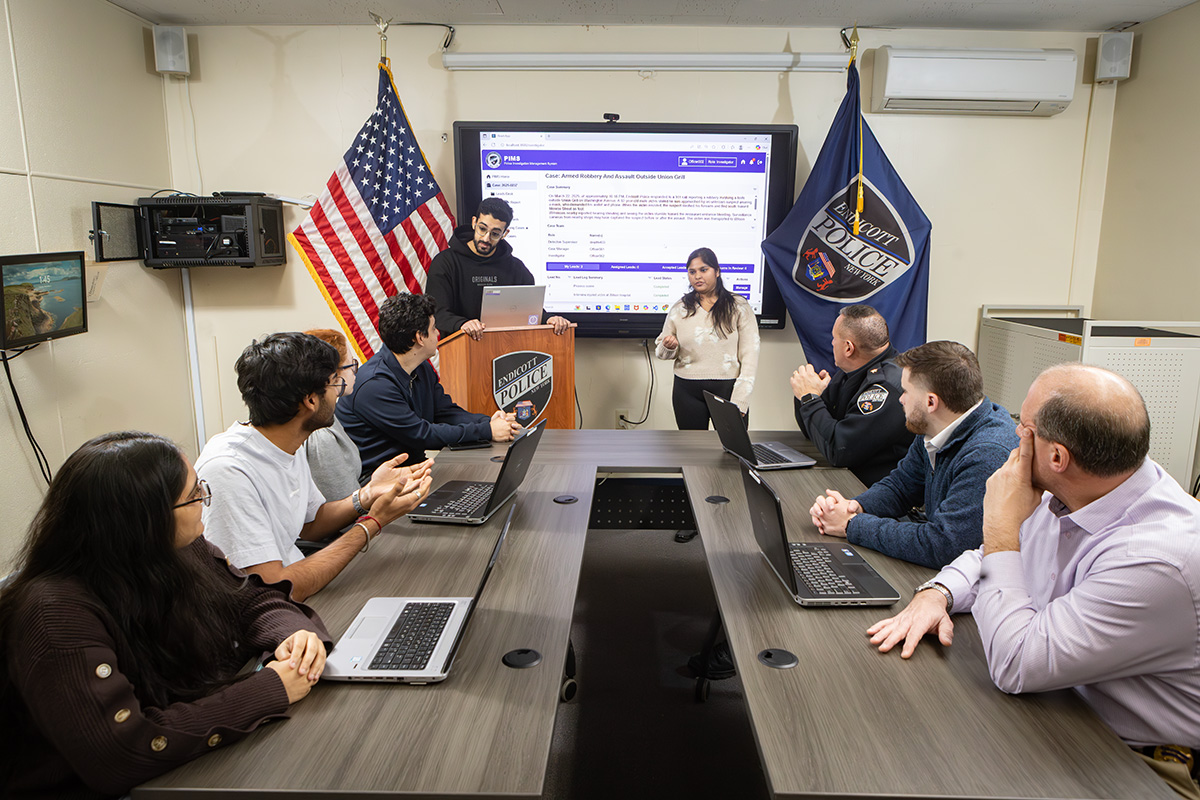 PhD student Mohammed-Khalil Ghali, MS ’24, and Shreya Agarwal, MS ’26, resent the Police Investigation Management System to, front to back at left, students Hemi Patel, Pranshu Desai, Sarah Escotto, and Abdelrahman Farrag; and front to back at right, Detectives Matt Brubaker and Jacob Harding and Chief Patrick Garey.