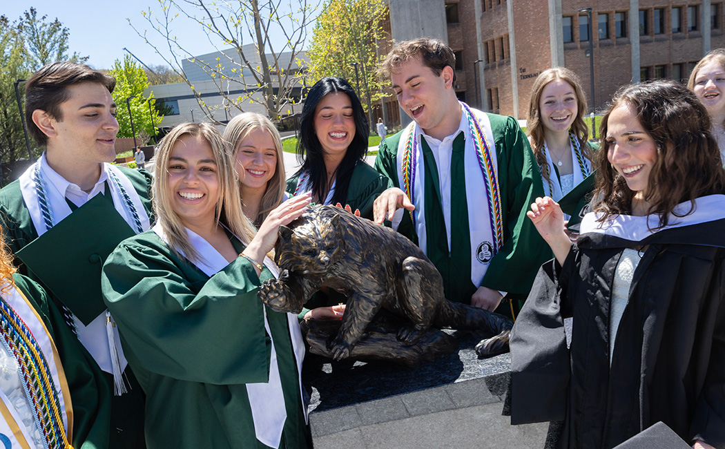 Graduating students with the new bronze statue of Bing the binturong on the Binghamton University campus.