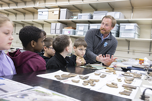 John Ferri, a project director at Binghamton University’s Public Archaeology Facility, examines archaeological discoveries with Glenwood Elementary School fourth-graders during a campus field trip in March. The facility, located in Science 1, often serves as one of the stops on the student tours.