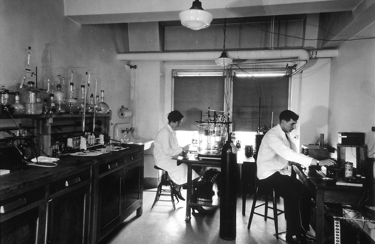 Two scientists sitting on stools in an interior wide shot of Chemical Laboratory, part of the Central Cancer Research laboratories.