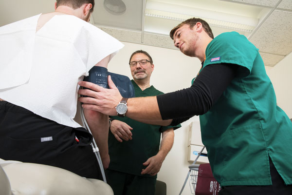 Dellazon Gilbert (center), a clinical instructor at the Decker School of Nursing, says he really enjoys working with Decker students. Here, he reviews John Meyer, a Baccalaureate Accelerated Track student, taking a blood pressure reading on a patient.