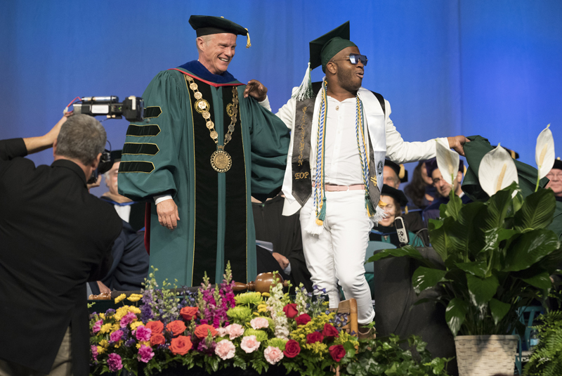 President Harvey Stenger laughs as School of Management student Desborne Villaruel tears off his Commencement robe and does a dance on the Events Center stage.