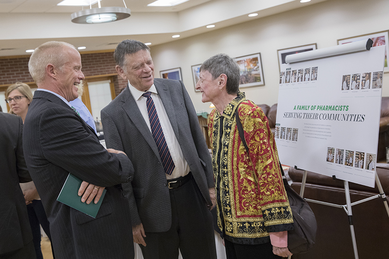 President Harvey Stenger speaks with Lisa Menner Brandt '66 and her husband, Dick, as they stand in front of a poster showing the many Menner family members who are pharmacists in Menner Brandt's native Austria.