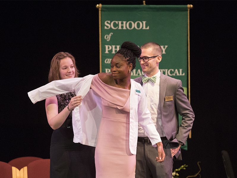Mavis Adu-Bonsu was the first student to receive a white lab coat from faculty Erin Pauling and William Eggleston during the inaugural School of Pharmacy and Pharmaceutical Sciences White Coat Ceremony held at the Watters Theater on Sept. 9.