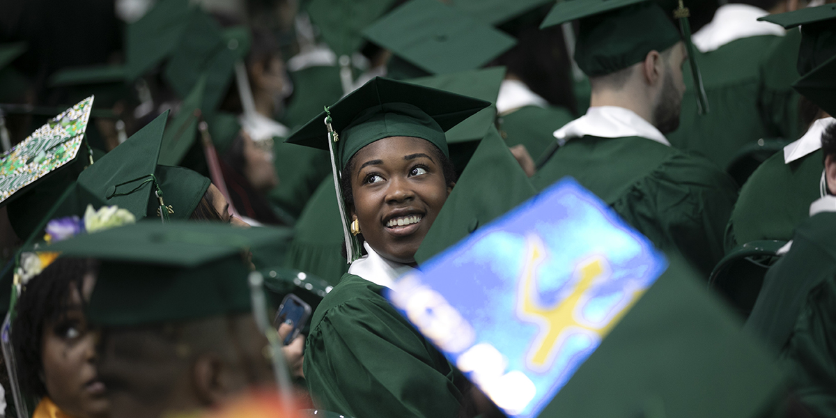 A graduate searches for family in the stands, amid a sea of mortarboards.