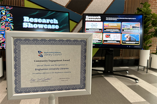 The SCRLC Certificate for Community Engagement is displayed in front of the Research Showcase touchscreen displays at Bartle Library.