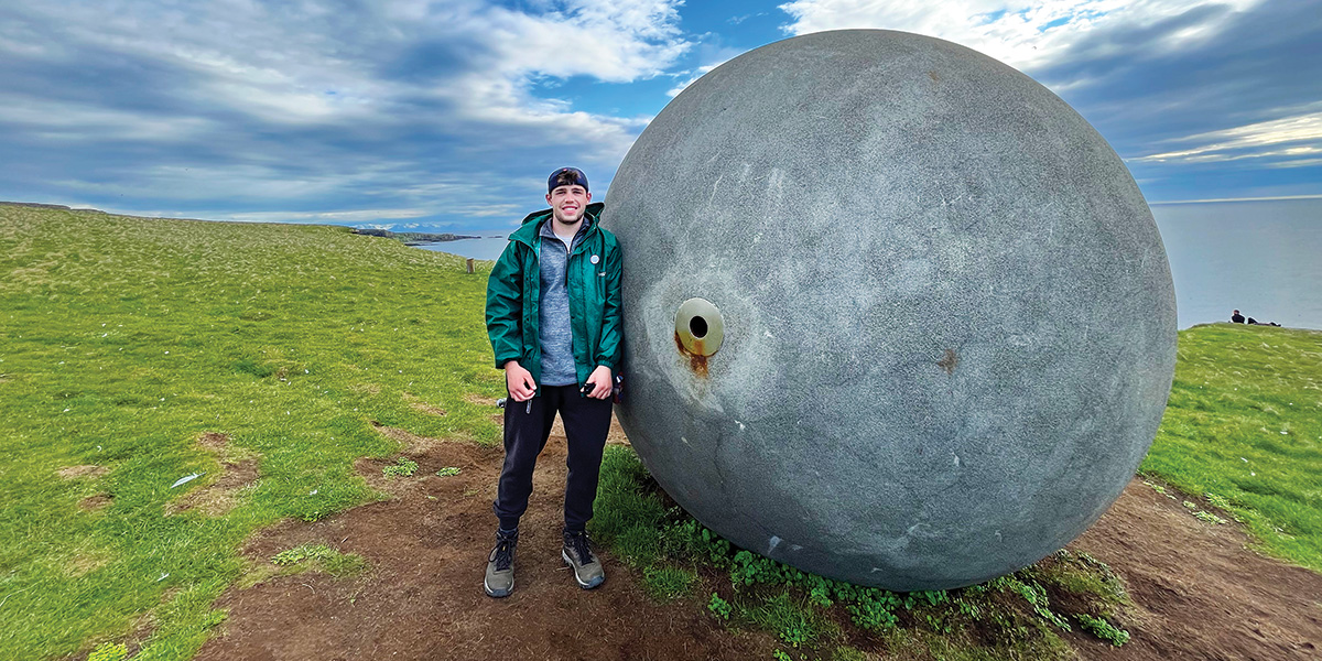 Lucas Grabowski ’23 stands next to the Arctic Circle Marker called “Orbis et Globus” (Latin for “Circle and Sphere”) on Grimsey Island in Iceland.