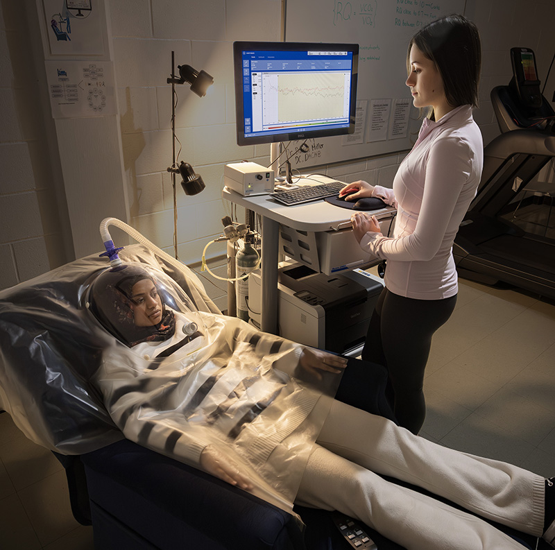 Mila Zlotnik, a member of the Laboratory Leadership Team, uses the metabolic cart to monitor Nema Sayeed, director of research operations, during resting metabolic rate testing. This test measures how the body uses energy at baseline.